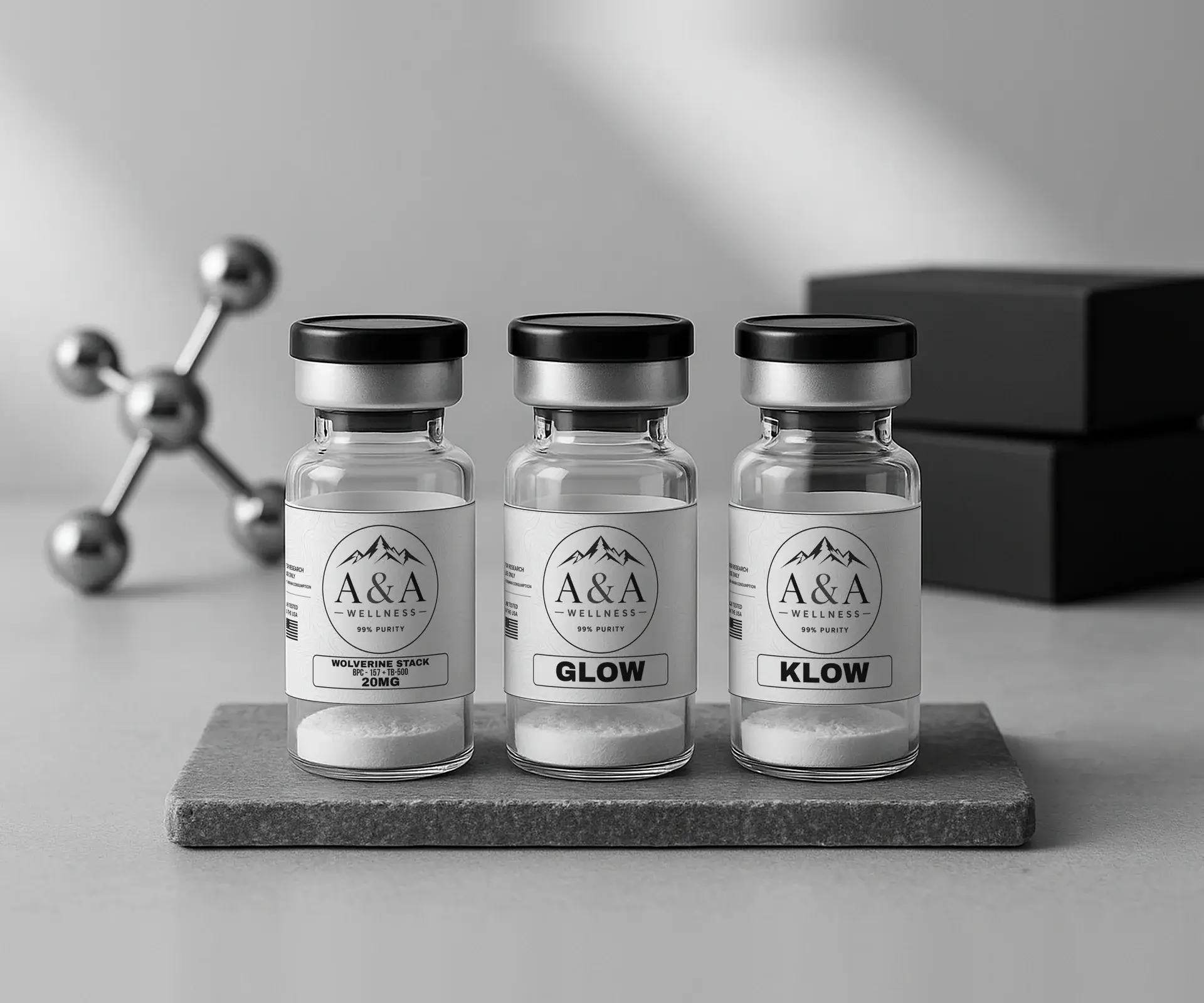 Wolverine, Glow and Klow A&A Wellness research blend vials on a gray stone slab with a chrome molecule model and black boxes behind